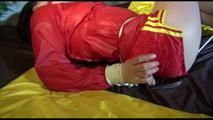 Lucy tied and gagged on bed wearing a red/yellow shiny nylon shorts and a red rain jacket (Video)