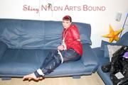 Jill tied, gagged and hooded infront of a sofa wearing a darkblue rain pants and a red rain jacket (Pics)