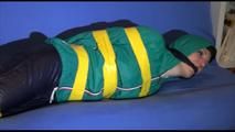 Mara tied, gagged and hooded with tape on a blue sofa wearing an blue/green rain combination (Video)