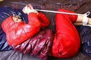 Pia tied and gagged on bed wearing a shiny red rain pants and a shiny red/purple down jacket (Pics)