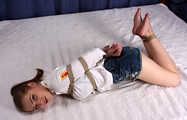 Barefoot Lisa in white shirt and jeans shorts, hogtied with hemp rope, wiggles and rolls on the bed