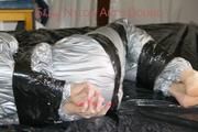 Pia tied and gagged with tape on a bed wearing a sexy silver rainwear combination (Pics) 