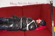 Lucy wearing a black shiny nylon rainh pants and a black down jacket tied and gagged on a sofa (Pics)