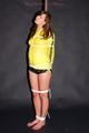 Alina tied and gagged to a pole in nylon shorts and yellow cagoule