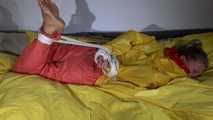 Watching Sandra  wearing an orange shiny nylon rain pants and a yellow shiny nylon rain jacket being tied and gagged on a bed with ropes and a clothgag (Video)